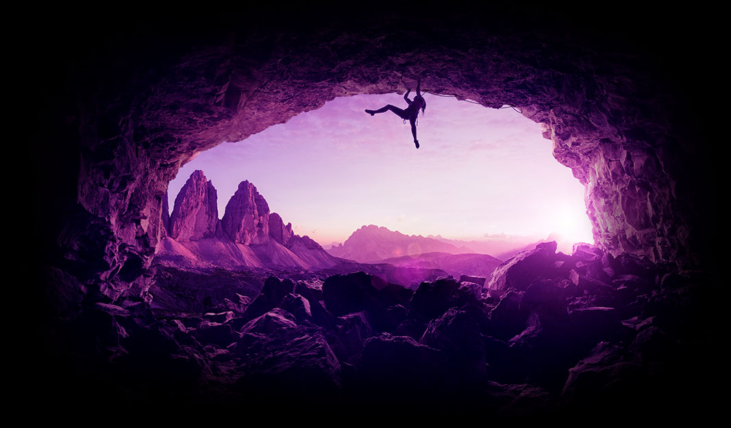 Image of a climber swinging from a mouth of a cave